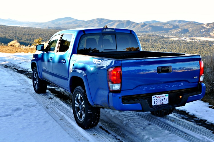 Rear view of blue Toyota Tacoma driving on snowy mountain trails