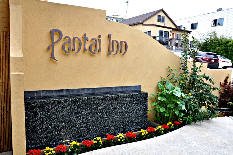 Pantai Inn sign with water feature and greenery