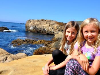 Zoë and Kaylee sitting on the cliffs at Point Lobos State Reserve on our family trip