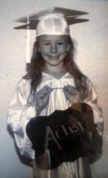 Zoë wearing a graduation outfit and holding a sign saying artist