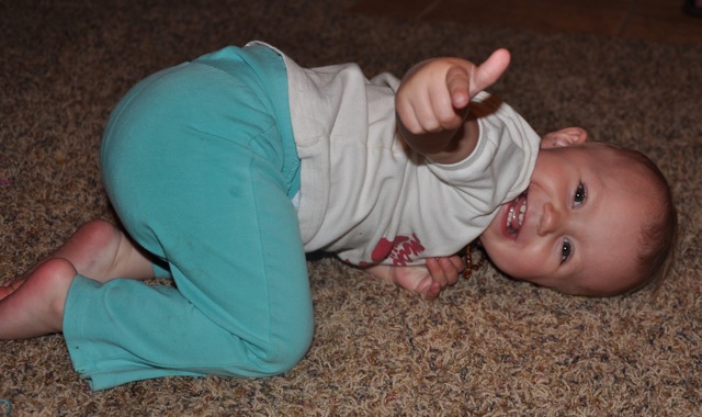 Toddler Kaylee pointing at the camera from a silly pose on the ground