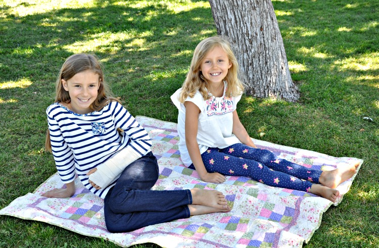 Zoë and Kaylee sitting on a quilt under a tree at the park