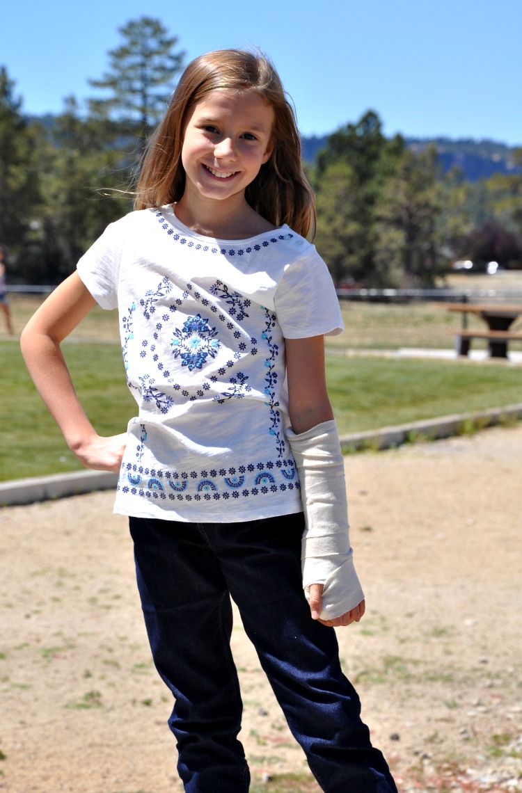 Zoë standing on a boulder with her hand on her hip and a broken arm