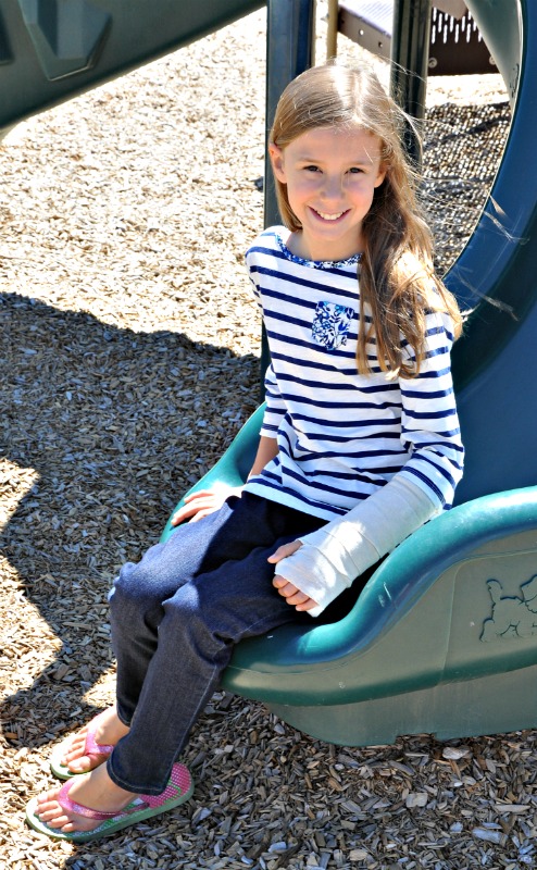 Zoë sitting on the bottom of the slide at the park