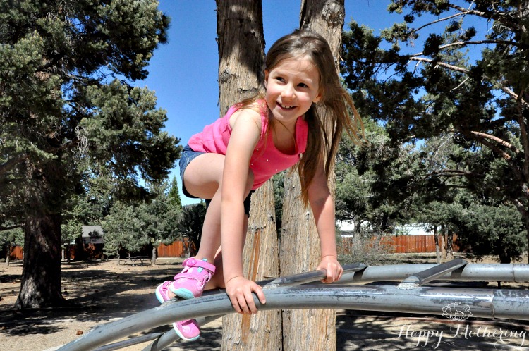 Zoë climbing on the rainbow bars at the park